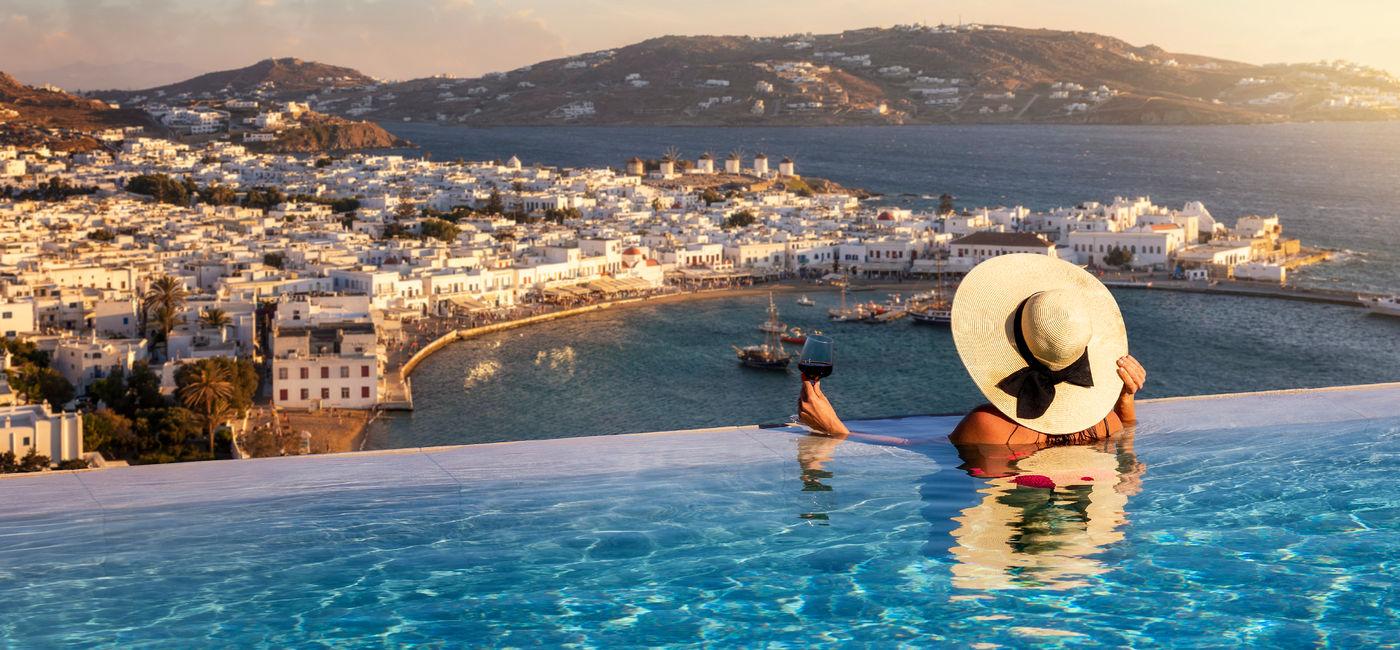 Image: Luxury traveler in an infinity pool with a glass of wine. (photo via iStock/Getty Images Plus/SHansche)