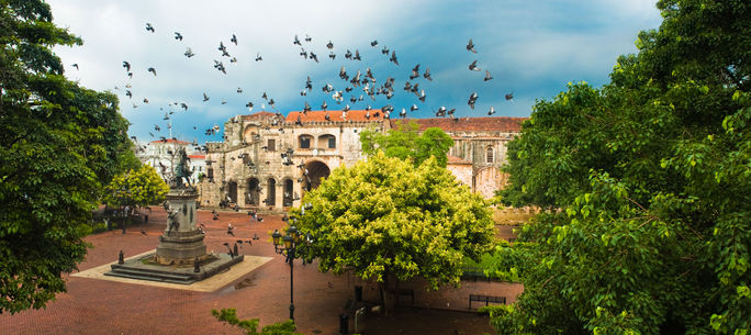 Doves flying over main square with Columbus statue, Santo Domingo, Dominican Republic (photo via 3dan3 / iStock / Getty Images Plus)