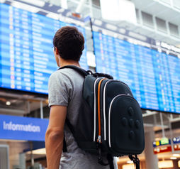 Young man with backpack in airport near flight timetable (Photo via furtaev / iStock / Getty Images Plus)